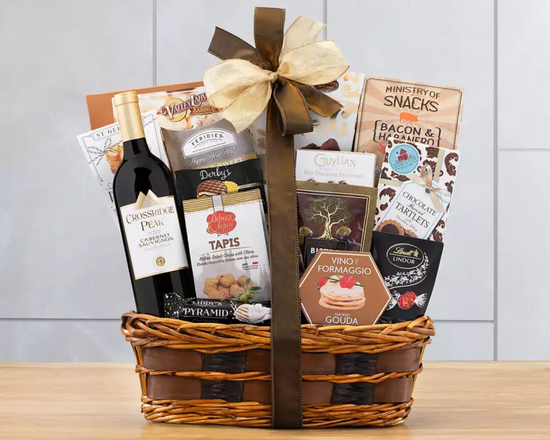 Gift basket with wine, snacks, and other items on a wooden surface. Gift basket with wine, snacks, and other items on a wooden surface.
