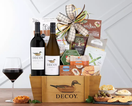 Gift basket with Decoy wine bottles, snacks, and a glass of red wine on a wooden surface. Gift basket with Decoy wine bottles, snacks, and a glass of red wine on a wooden surface.
