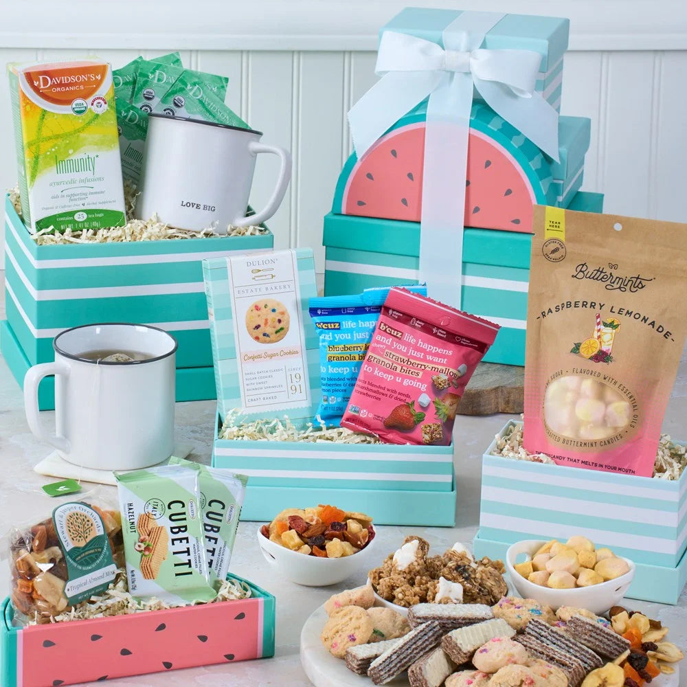 Assorted snacks and treats in colorful gift boxes with mugs and bowls on a white surface.