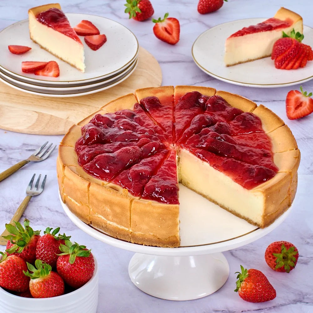 Strawberry cheesecake on a white cake stand with slices served on plates, surrounded by fresh strawberries.