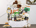 White metal Gift basket filled with various food items on a wooden surface.