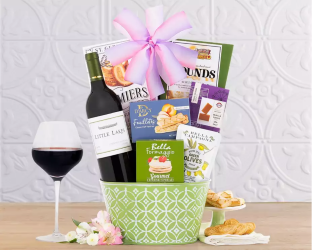 Wine gift basket with a bottle of wine, snacks, and a glass of red wine on a wooden table.
