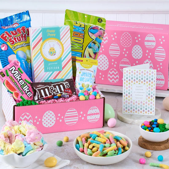 Assorted candy and snacks in a pink box with Easter-themed packaging on a wooden table.
