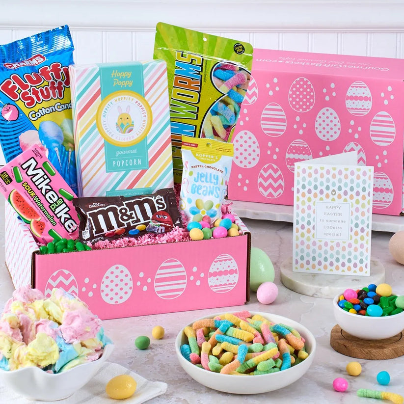 Assorted candy and snacks in a pink box with Easter-themed packaging on a wooden table.