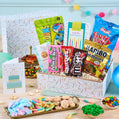 Assorted candy and snack box with birthday cards on a table.