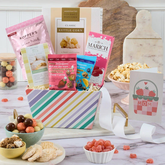 Gourmet gift basket with snacks and a 'Mom' card on a wooden table.