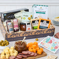 Gourmet gift box with various food items including cheese, olives, and meats on a table.