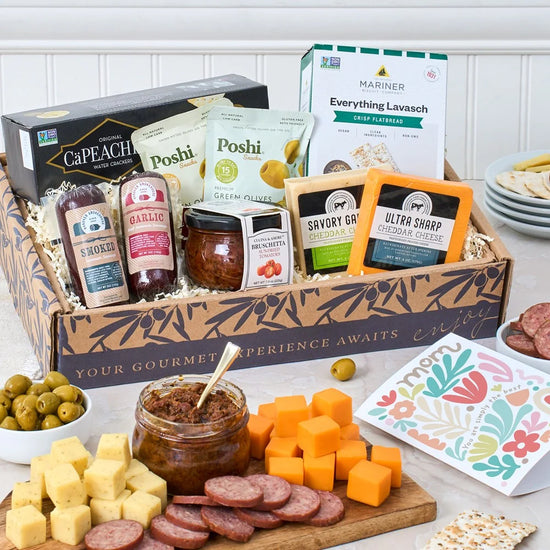 Gourmet gift box with various food items including cheese, olives, and meats on a table.